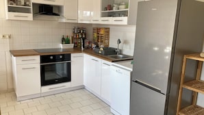 A modern kitchen with white cabinetry, a stainless steel refrigerator, a built-in oven, and a dishwasher. - Cozy family apartment in the heart of Görlitz, also suitable for fitters (Görlitz)
