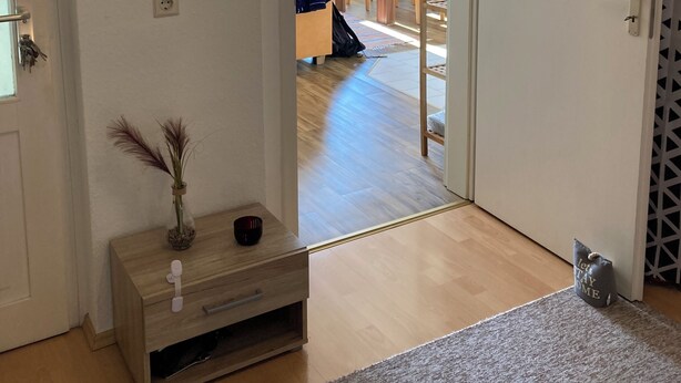 A hallway leading to a dining area with a wooden table and chairs, a small wooden cabinet with a vase, and a grey rug on the floor. - Cozy family apartment in the heart of Görlitz, also suitable for fitters (Görlitz)