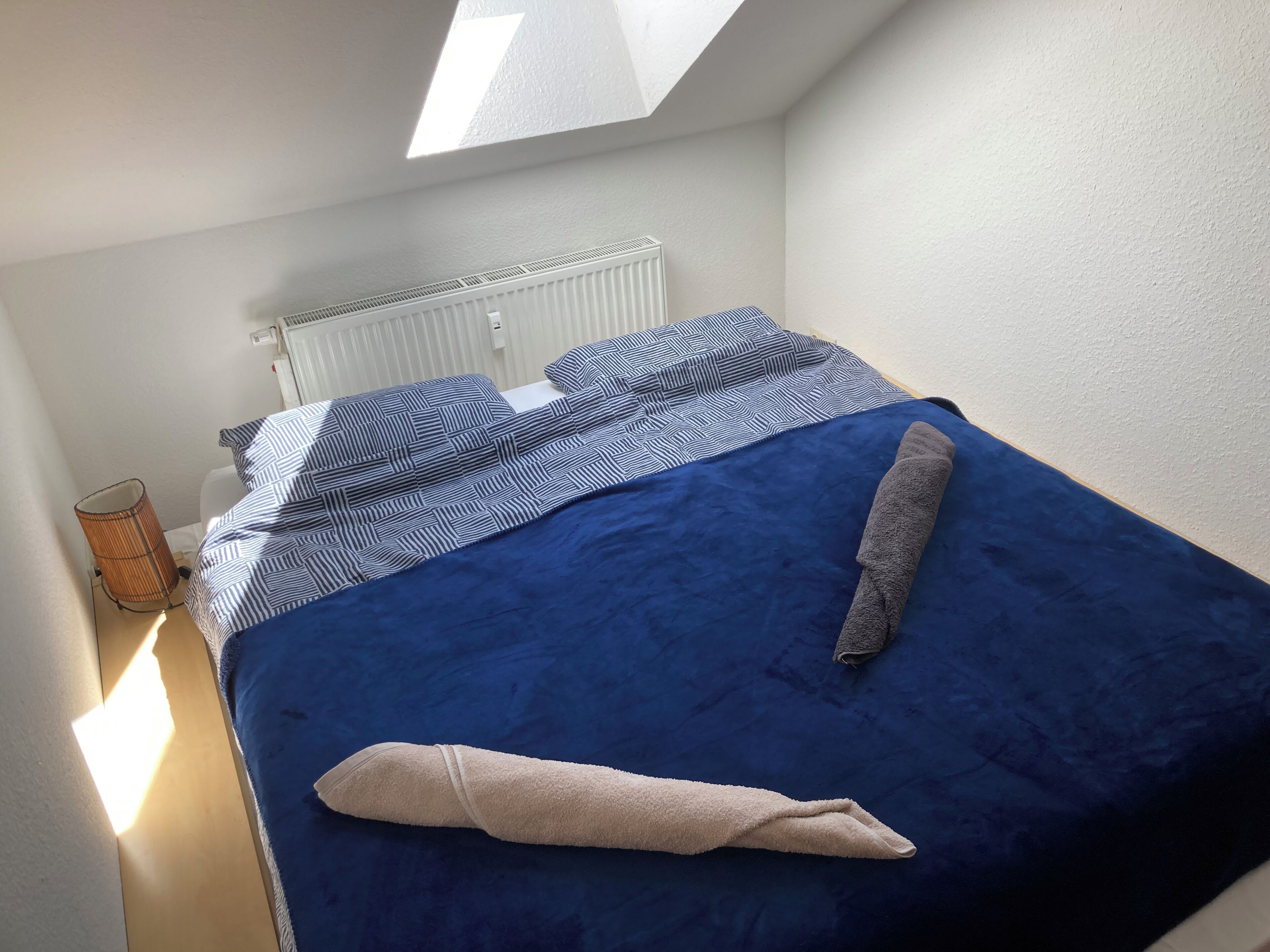 A small, neatly arranged bedroom with a bed, a radiator, and a window.