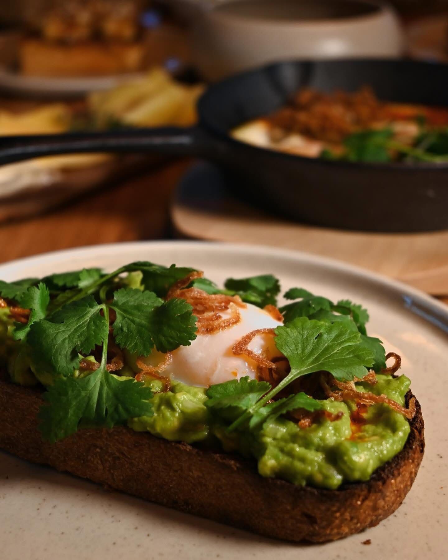 Un sándwich con aguacate y huevo escalfado sobre una rebanada de pan, adornado con cilantro y cebollas fritas.