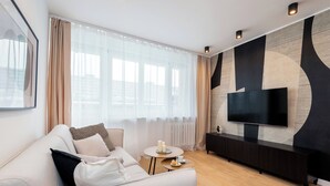 Un salon moderne avec un canapé, une table basse, un téléviseur et une grande fenêtre avec des rideaux.