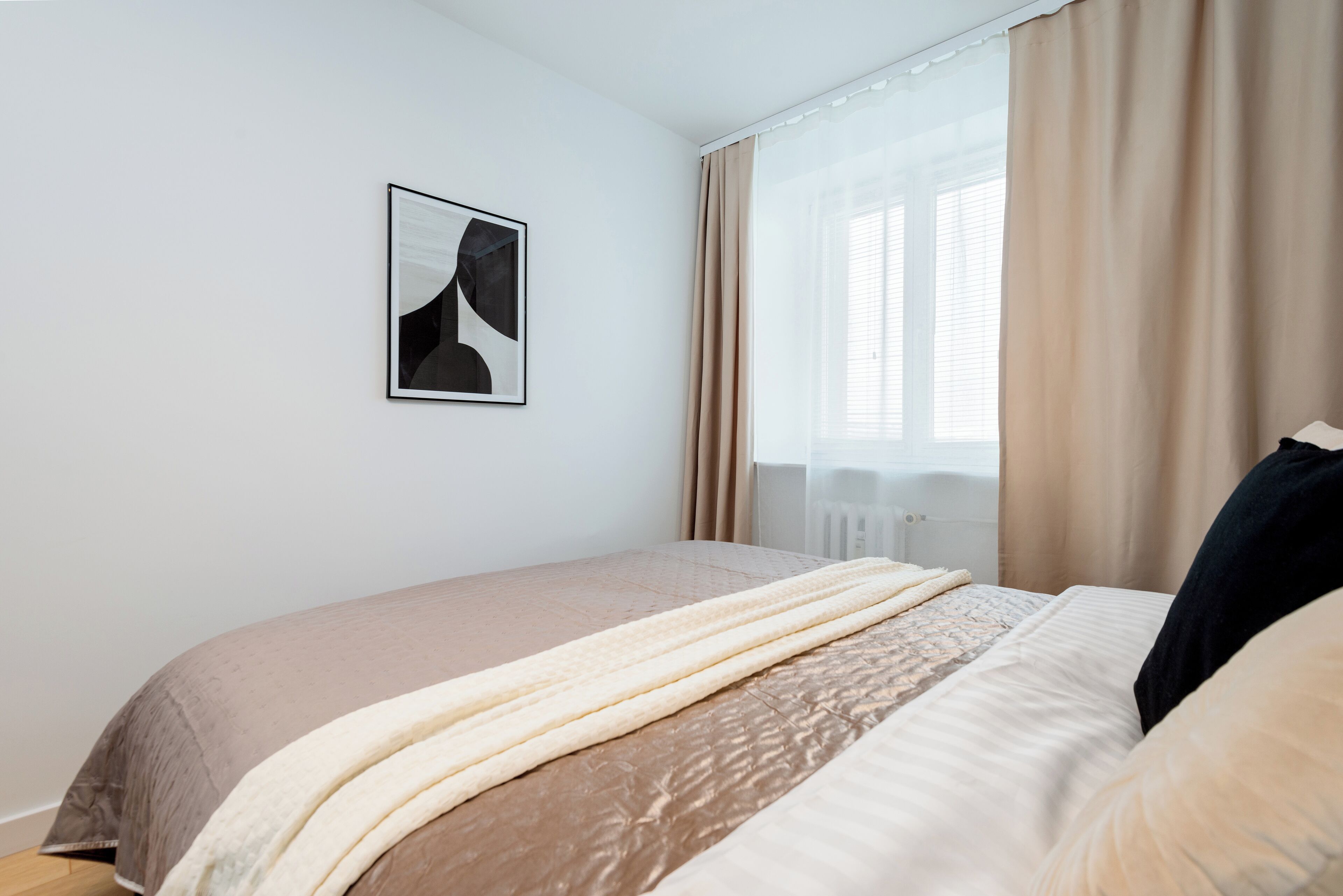 A bedroom with a bed, a window with curtains, and a framed picture on the wall.
