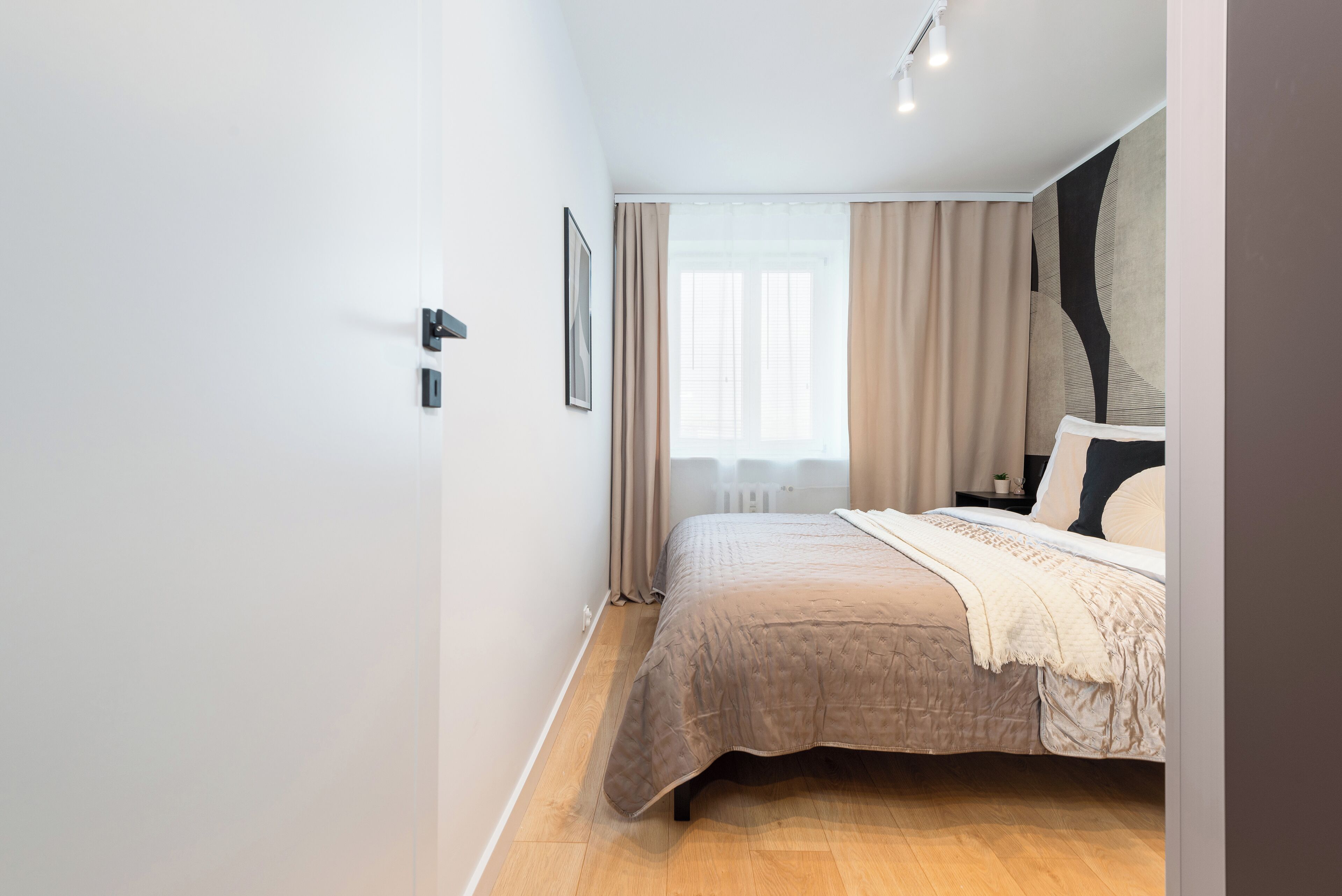 A bedroom with a bed, curtains, a window, and a wall-mounted light fixture.