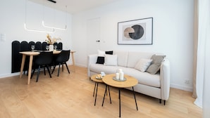 Un salon moderne comprenant un canapé, une table à manger avec des chaises, une table basse et une œuvre d’art encadrée accrochée au mur.