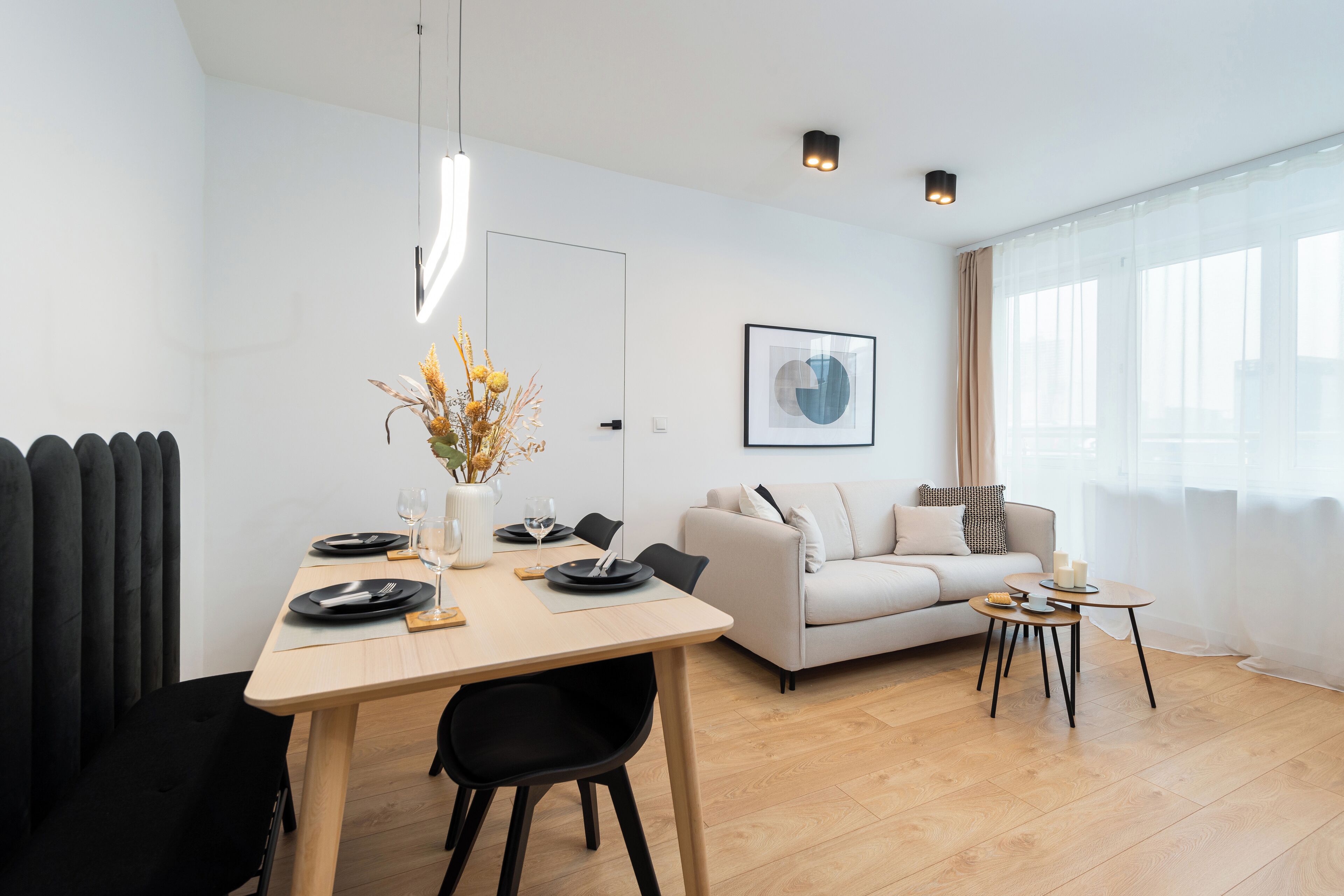 A modern living room with a dining area, featuring a sofa, a coffee table, and a dining table set with plates and glasses.