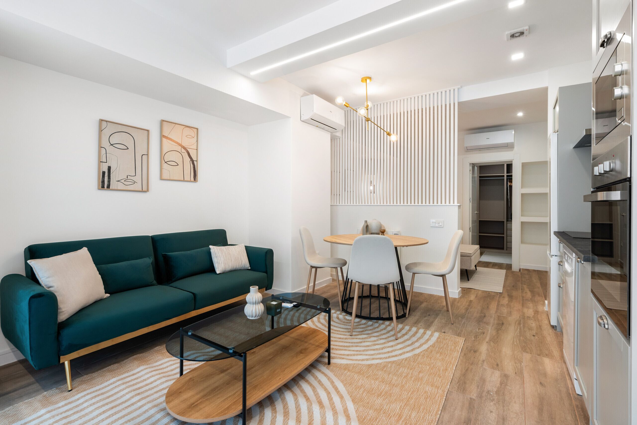 A modern living room with a green sofa, a glass coffee table, and a dining area with a round table and chairs.