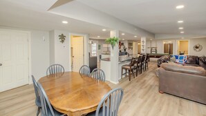 A spacious living area with a wooden dining table, blue chairs, a brown leather sofa, and a kitchen in the background. - Spacious 6-bedroom house in enjoyable PK with Waterfront Access Near Rocker-B (Graford)