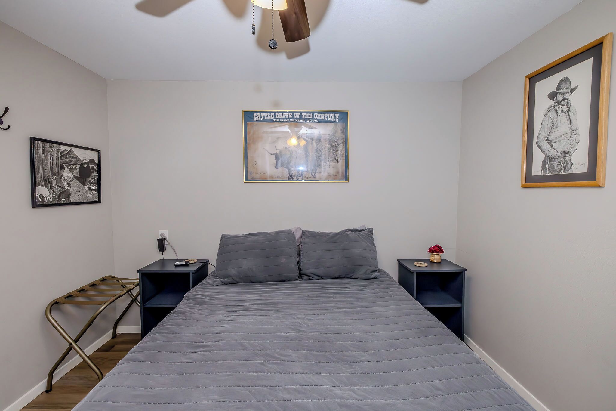 A bedroom with a bed, two nightstands, a wall-mounted lamp, and framed artwork.