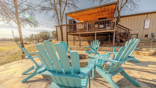 A covered outdoor area with Adirondack chairs and a table, a wooden deck, and a building with a balcony. - Spacious 6-bedroom house in enjoyable PK with Waterfront Access Near Rocker-B (Graford)