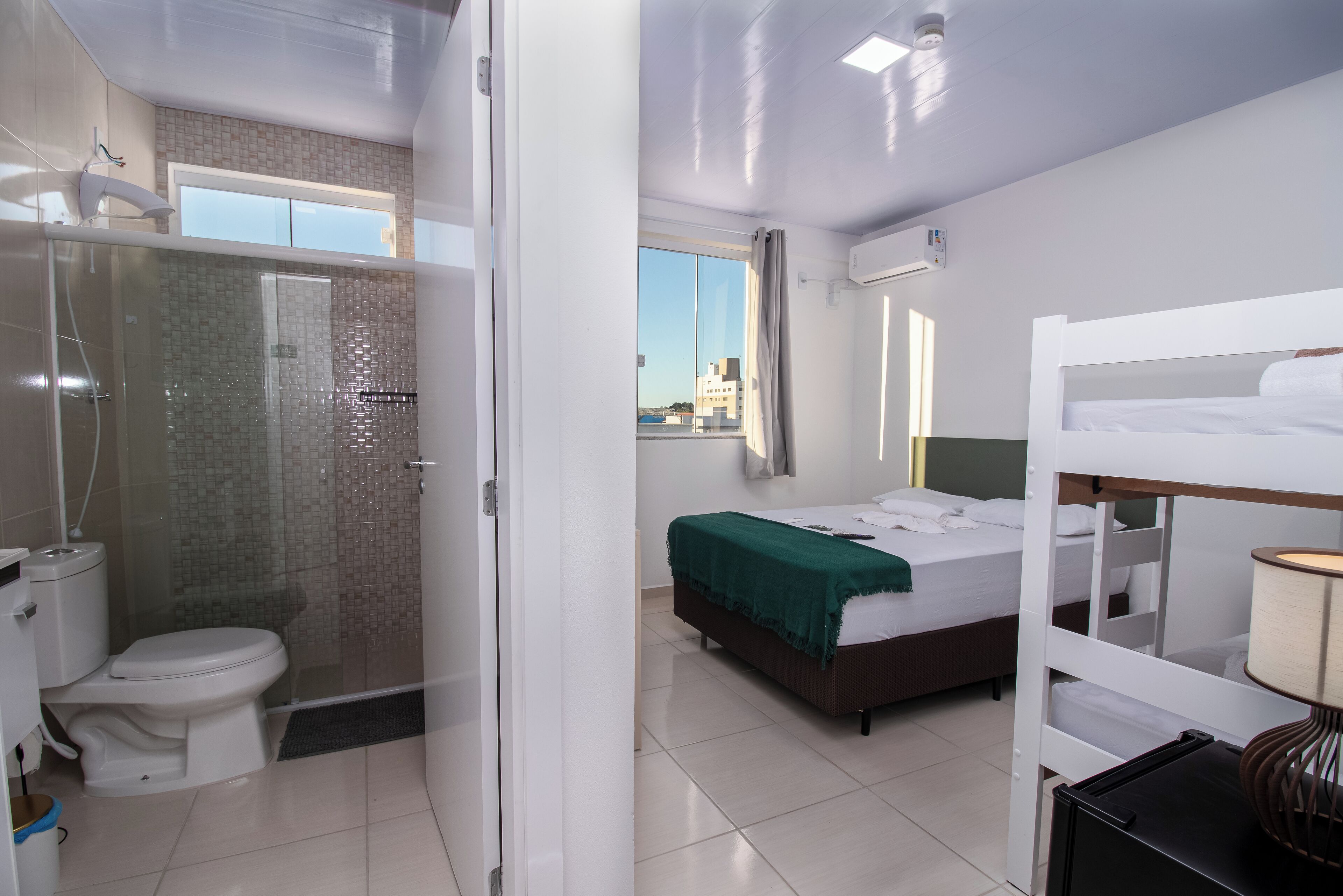 A hotel room with a shower, toilet, bed, and a view of the city.