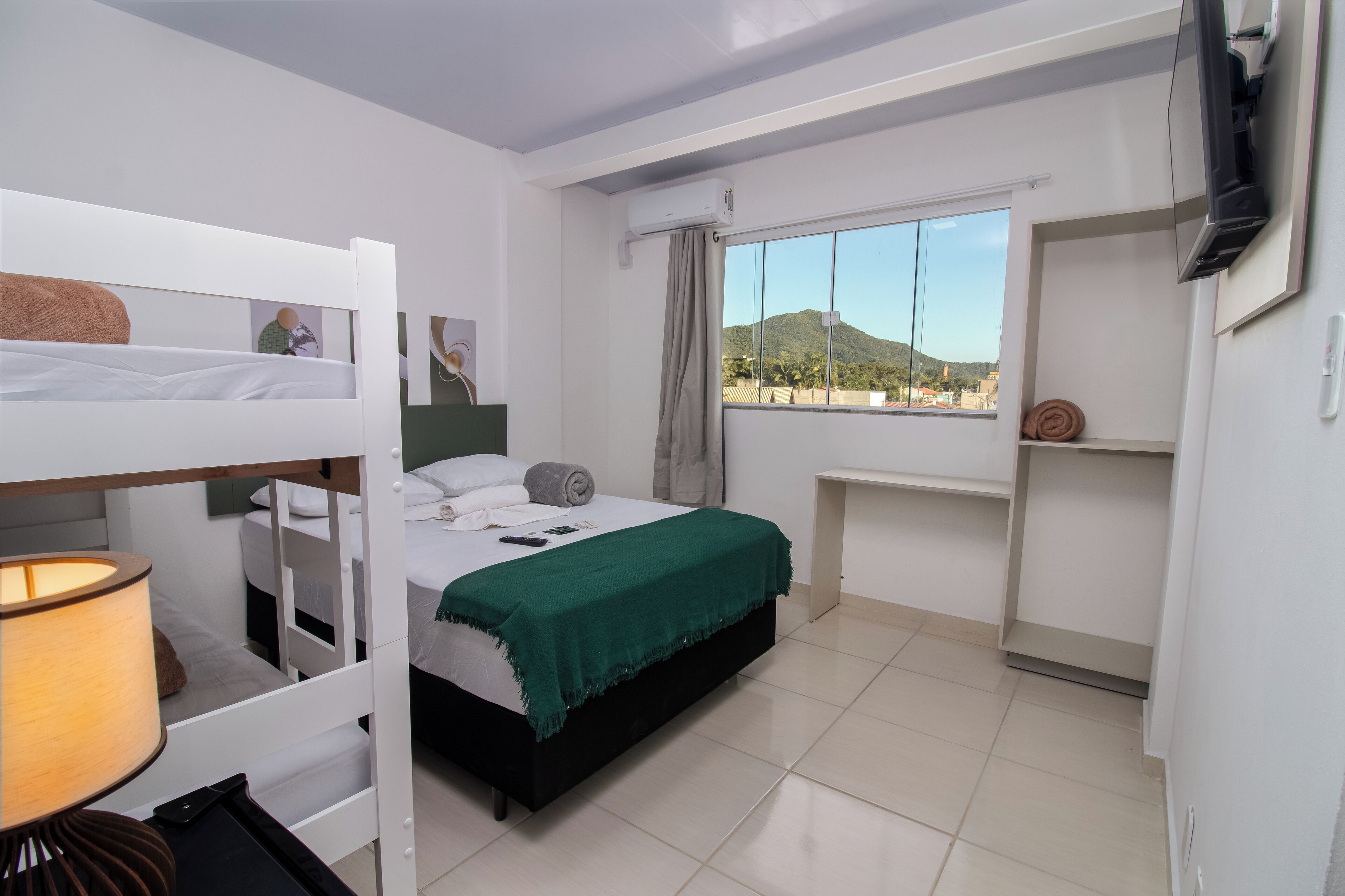 A bedroom with bunk beds, a desk, a TV, and a window with a mountain view.