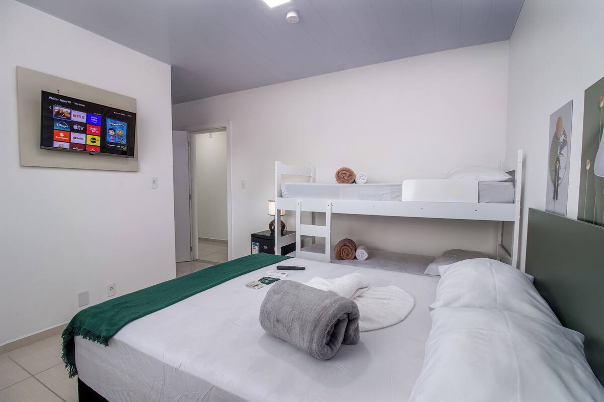 A hotel room with a bunk bed, a flat-screen TV mounted on the wall, and a green throw blanket on the bed.