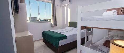 Habitación de hotel compacta con literas, una cama individual con una manta verde, una ventana con cortinas y vistas a la ciudad.