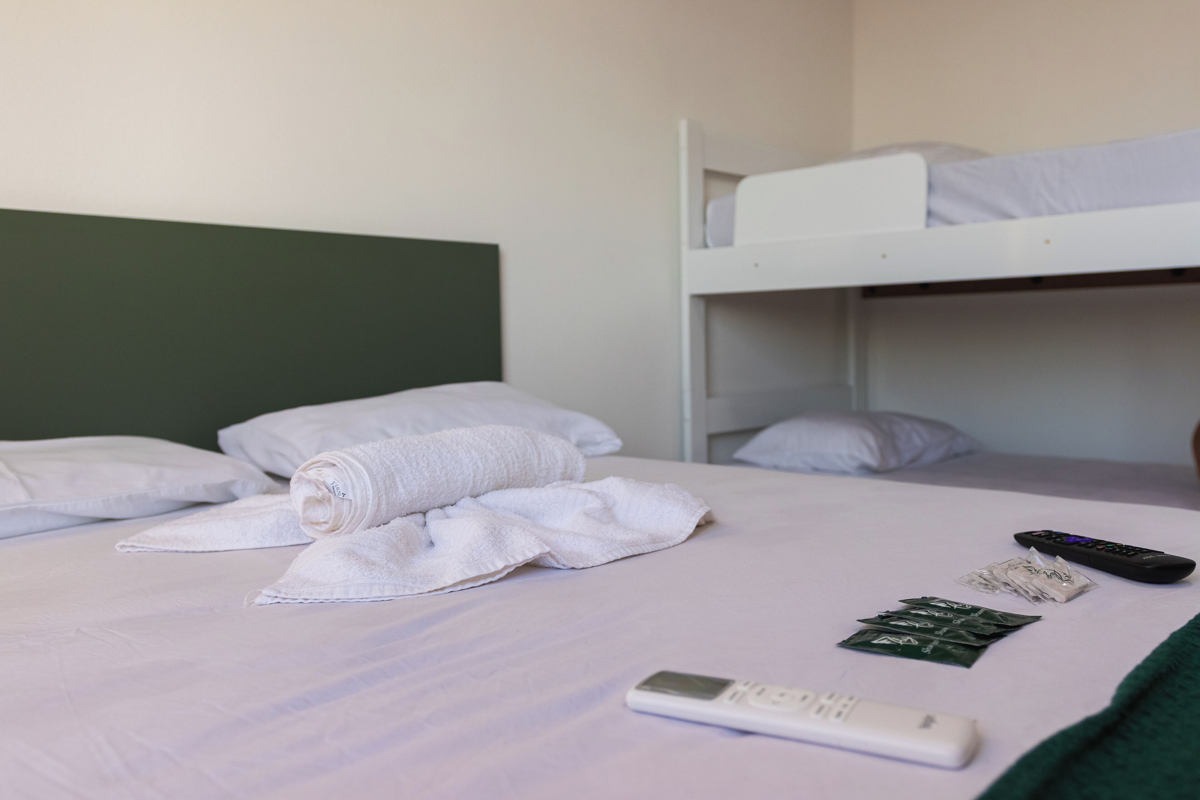 Une chambre d’hôtel avec un lit simple, un lit superposé et une télécommande posée sur le lit.
