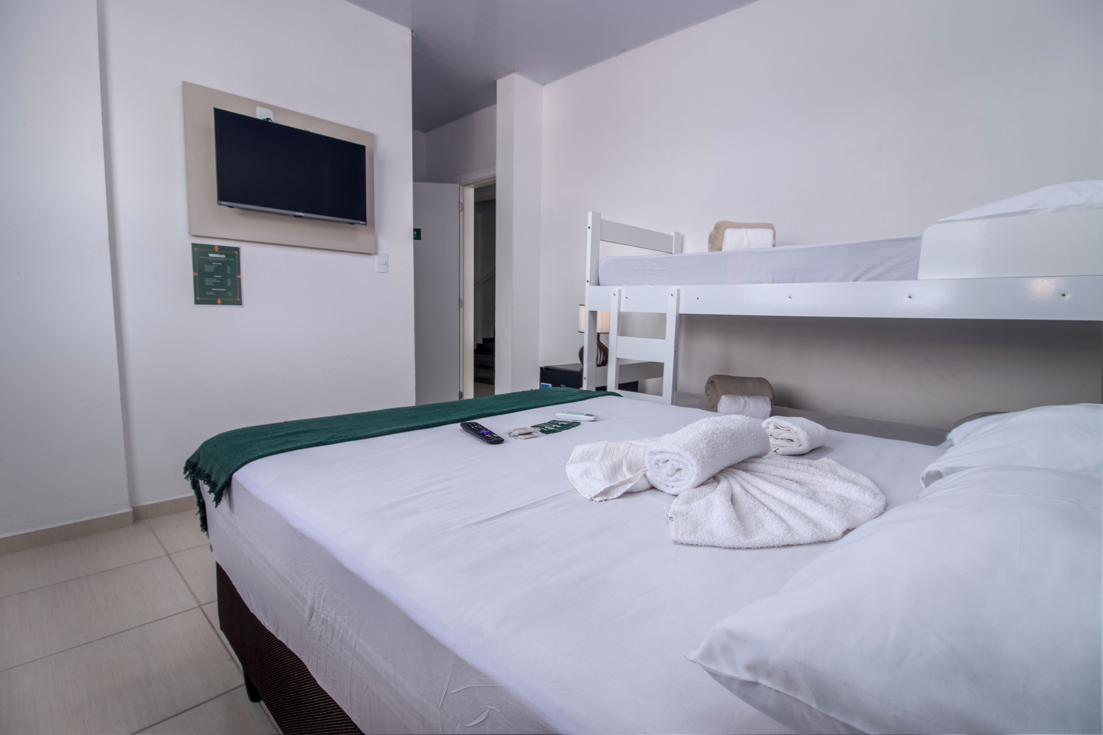 A hotel room with a single bed, a TV mounted on the wall, a green towel, and a remote control on the bed.