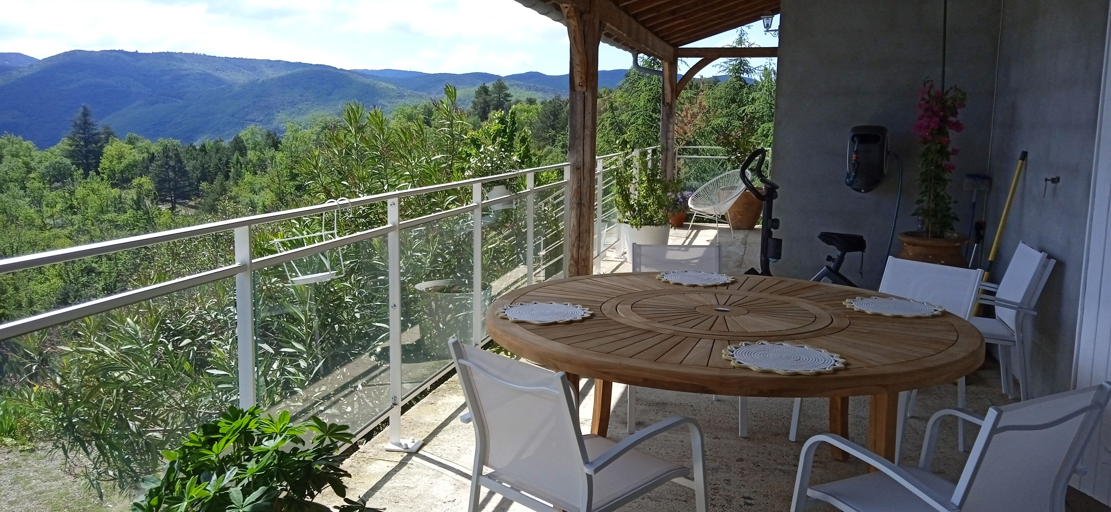 A wooden table with white chairs on a balcony with a metal railing, overlooking a mountainous landscape.