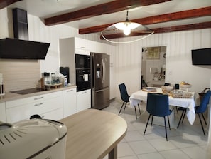 Een moderne keuken met witte kasten, roestvrijstalen apparatuur en een eethoek met blauwe stoelen en een witte tafel.