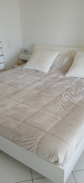 Een bed met een gewatteerde beige dekbedovertrek, witte kussens en een wit hoofdbord.