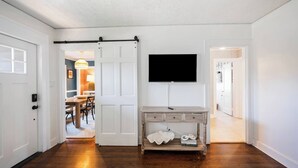 A hallway with a sliding door leading to a dining area, a mounted TV, and a wooden console table with decorative items.
