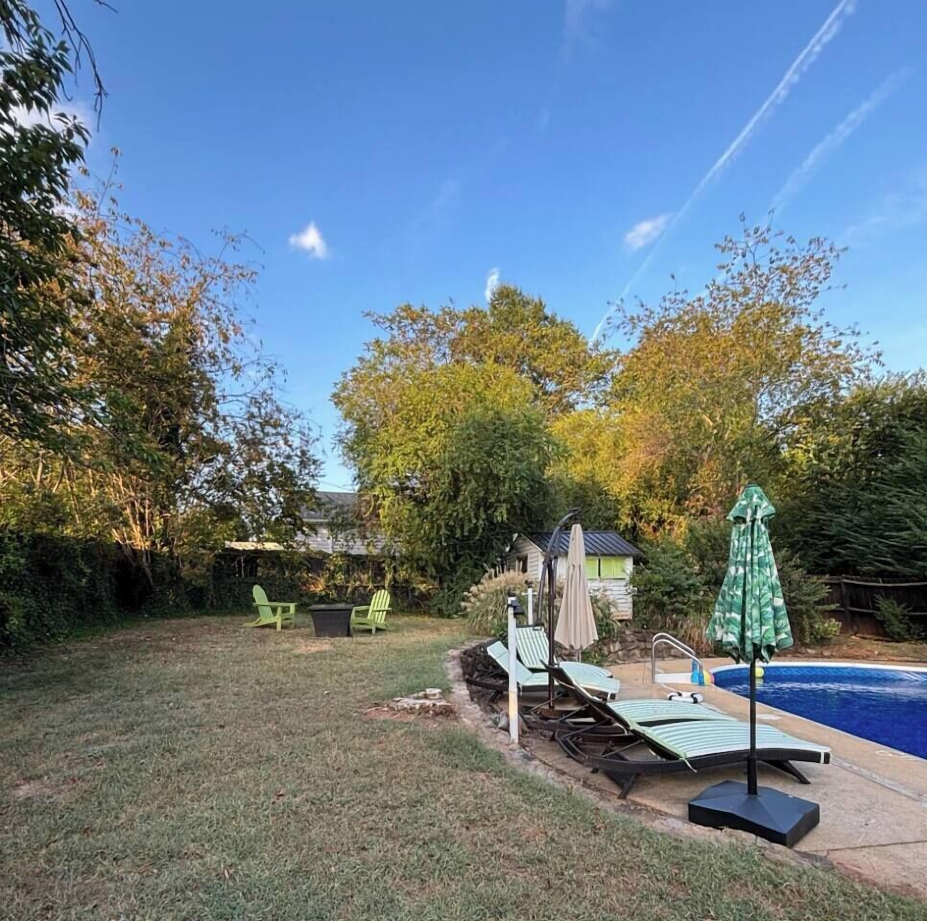 A backyard with a swimming pool, green lawn chairs, and a small shed.