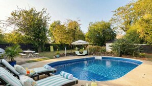 A backyard with a swimming pool, lounge chairs, a table, and a covered seating area.
