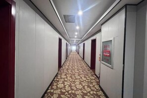 A hotel corridor with a patterned carpet, doors on both sides, and a sign on the wall.