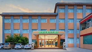 Un hotel con fachada moderna, una entrada destacada y un estacionamiento con varios coches.
