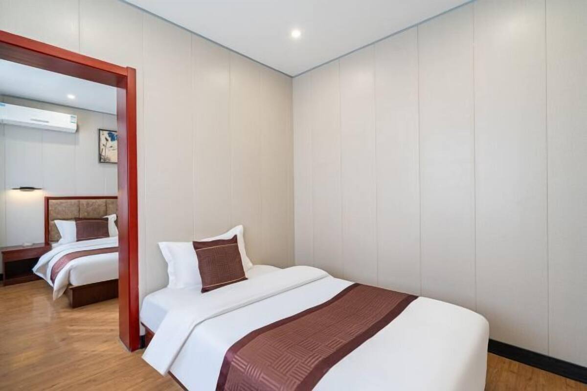 A hotel room with a large bed, a wooden floor, a mirror, and a wall-mounted air conditioner.