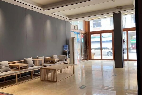 A modern lobby with seating areas, a reception desk, and a view of the street through glass doors.