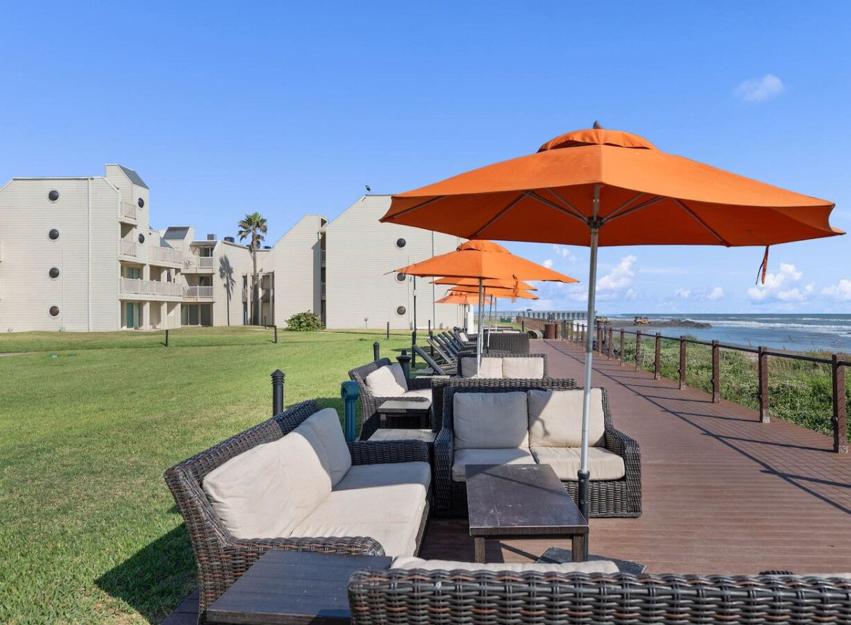 Un patio frente al mar con mobiliario de mimbre y sombrillas naranjas, con vista al océano.