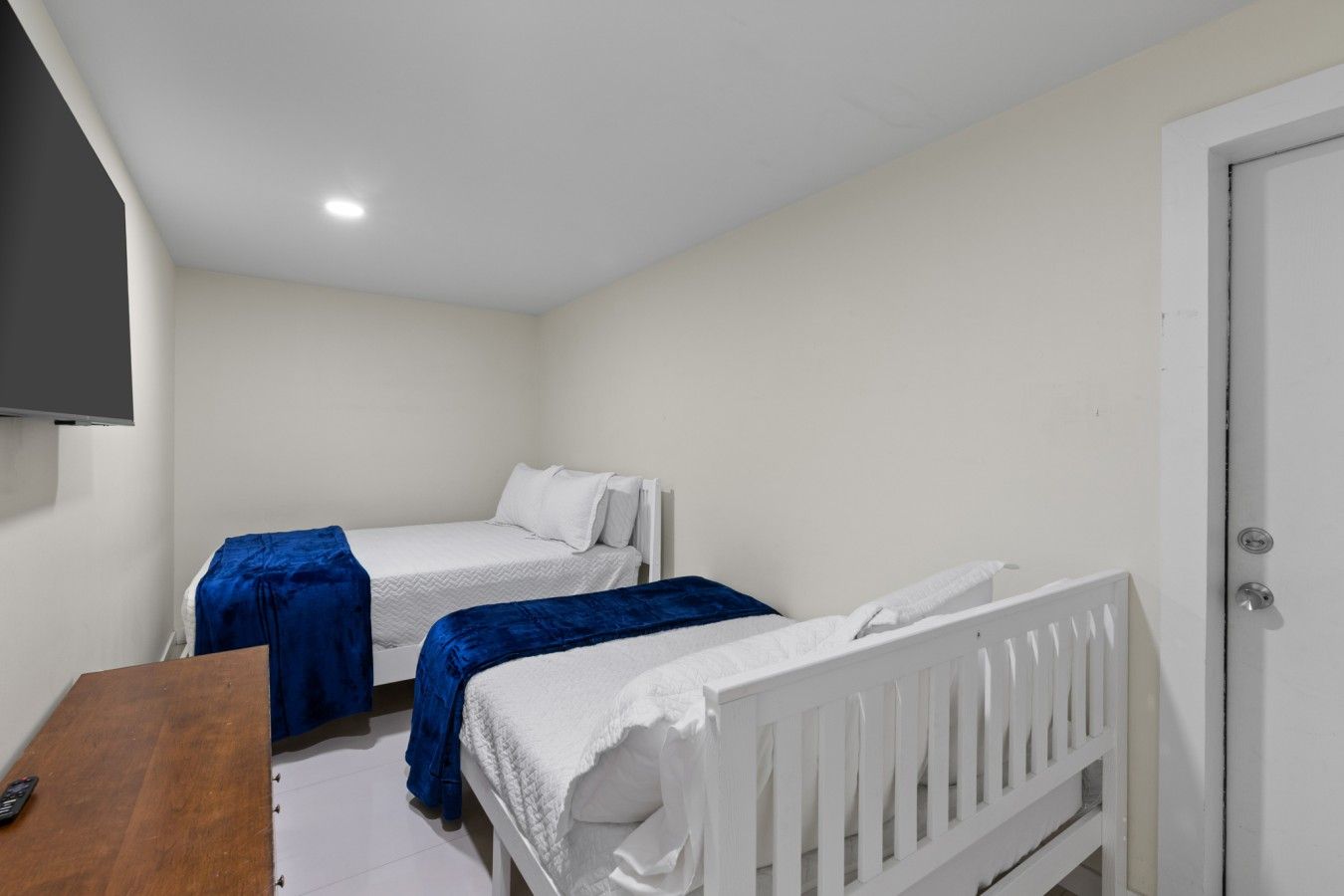 A bedroom with two single beds, a wooden desk, and a white door.