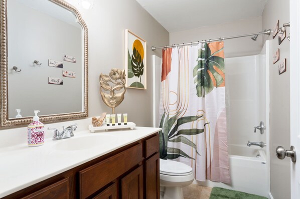 A bathroom with a large mirror, a vanity with toiletries, a toilet, a shower with a curtain, and a bathtub.