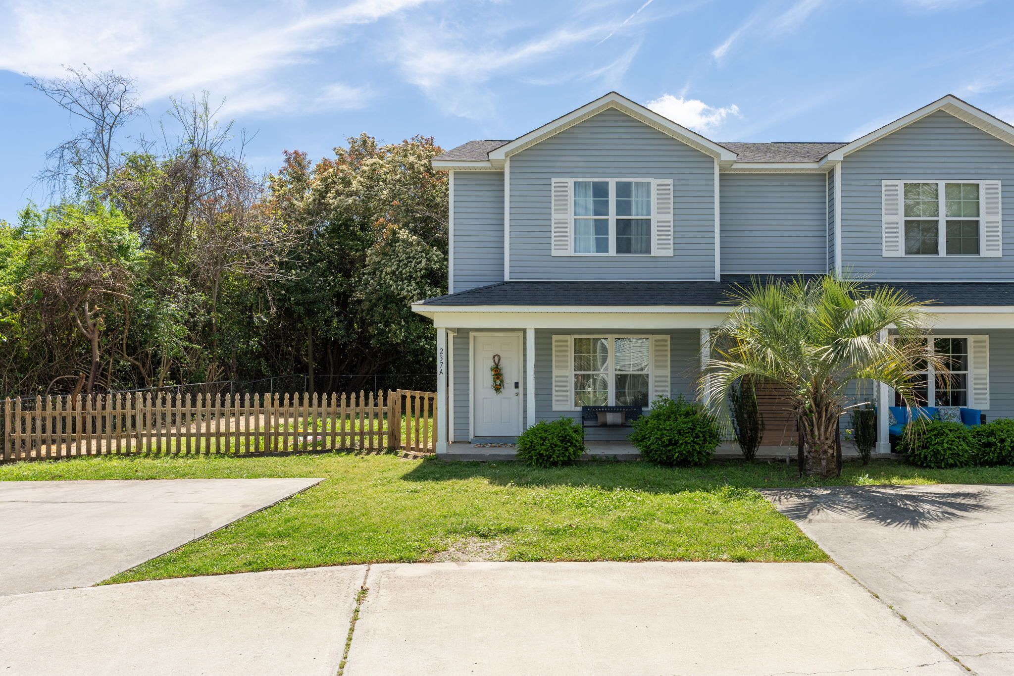 A two-story residential building with a front porch, a small garden, and a wooden fence.
