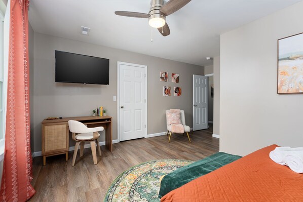 A bedroom with a bed, a desk, a chair, a television, and a door. - Modern 3 Bedroom townhome, Sleeps 8! 5 minutes to UNCW & Wrightsville beach. (Wilmington)
