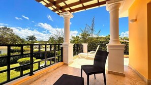 A balcony with white columns, a black chair, and a view of the surrounding greenery.
