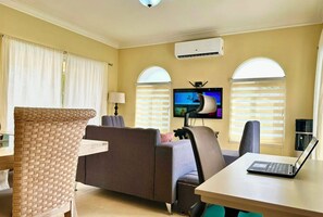 Een woonkamer met een bank, een stoel, een tafel met een laptop en een televisie aan de muur.