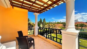 Een balkon met een pergola, witte zuilen en uitzicht op een woongebied met huizen en groen.