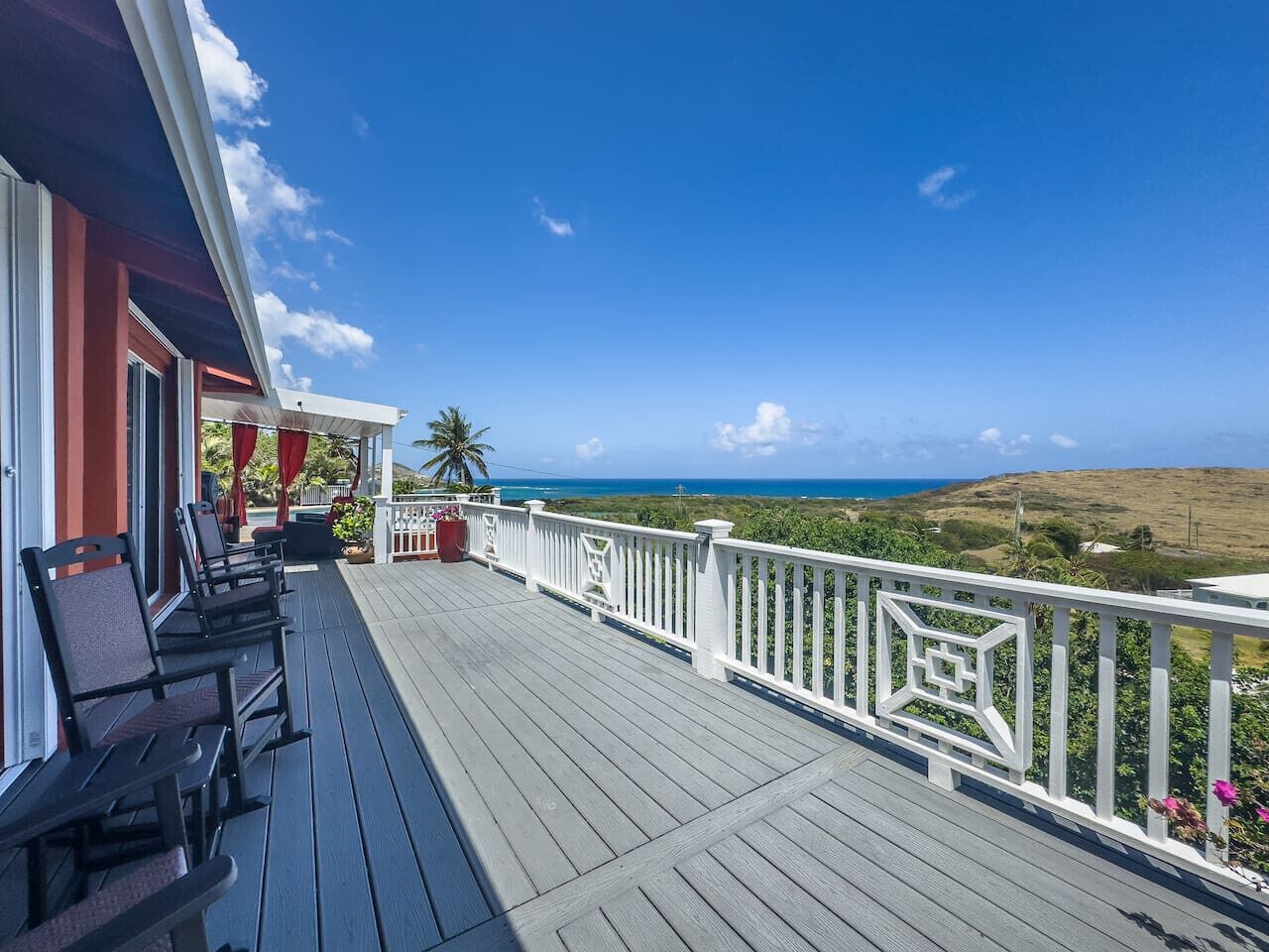 A wooden deck with chairs and a railing overlooking a coastal view.
