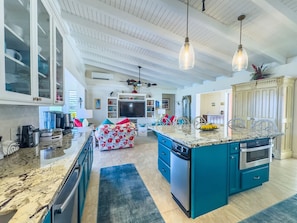 Una cocina amplia con una isla grande, un comedor y un televisor al fondo.