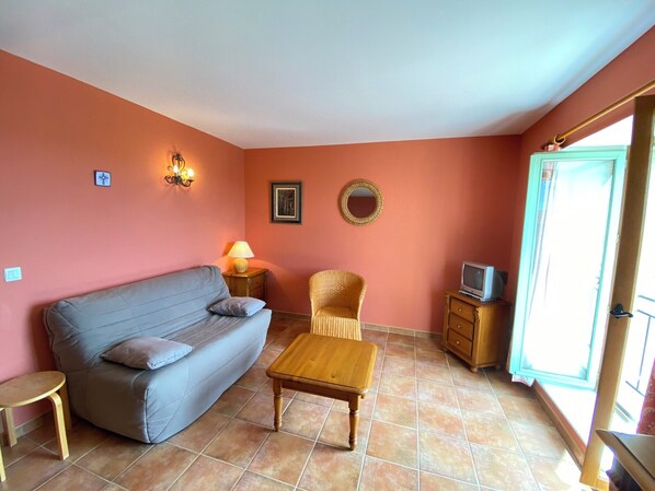 A living room with a sofa, a wooden coffee table, a wicker chair, a TV, and a small table. - 04B4 : Beautiful studio in a mas provençal - pool (Brunet)
