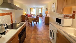 Une cuisine compacte équipée d’une cuisinière, d’un four à micro-ondes et d’un lave-linge. Elle comprend un coin repas avec une table et des chaises. Les murs et le sol de la cuisine sont recouverts de carrelage.