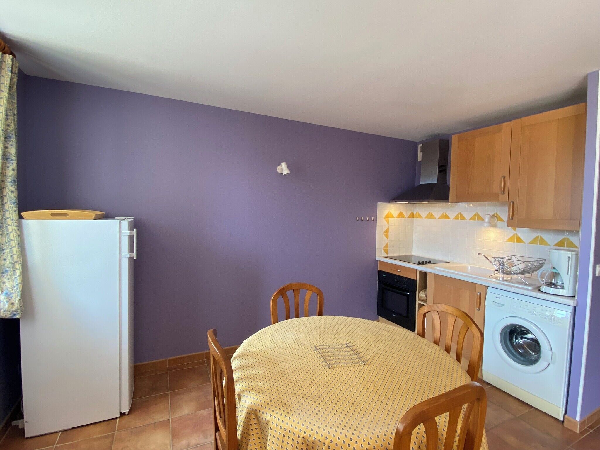 Une cuisine compacte équipée d’un lave-linge, d’une table à manger avec des chaises et d’un réfrigérateur.