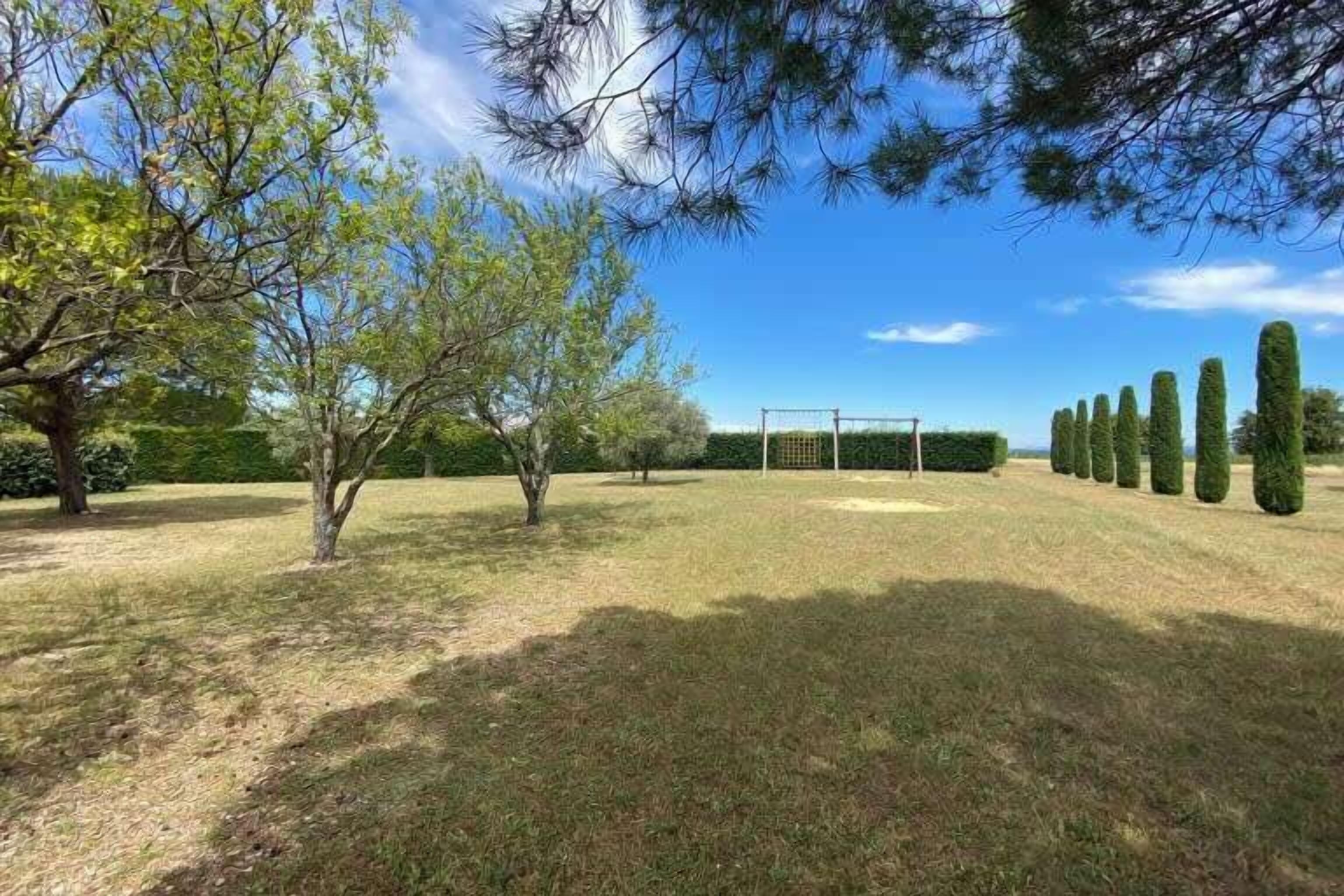 Zona verde bien cuidada con un arco de fútbol, rodeada de árboles y setos.