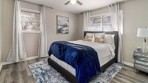 Een slaapkamer met een bed, een plafondventilator, een nachtkastje en een raam met gordijnen.