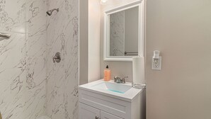 Een badkamer met een betegelde douchewand van marmer, een witte wastafel met een spiegel erboven en een handdoekdispenser.