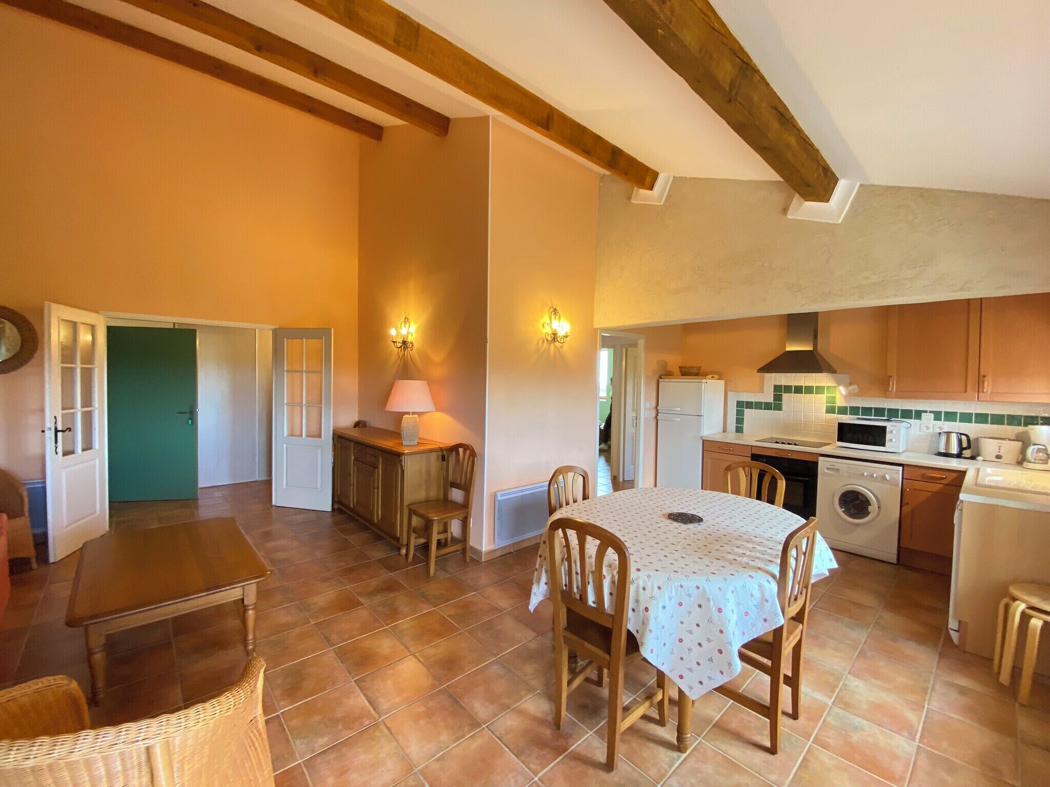 A cozy kitchen with a dining area, wooden beams, a washing machine, and a table with chairs.