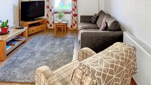 A living room with a sofa, a TV, a small table with a plant, and a window with curtains. - 2 bedroom accommodation in Cellardyke, near Anstruther (Cellardyke, near Anstruther)