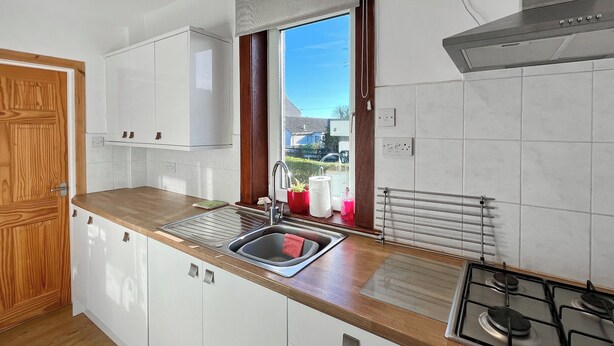 A modern kitchen with white cabinets, a stainless steel sink, a gas stove, and a window with a view of houses. - 2 bedroom accommodation in Cellardyke, near Anstruther (Cellardyke, near Anstruther)