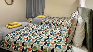A double bed with patterned bedding, a small round mirror, and a grey curtain. - 2 bedroom accommodation in Cellardyke, near Anstruther (Cellardyke, near Anstruther)