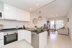 A modern kitchen with integrated appliances, a dining area with a sofa and table, and a view of the outdoors. - Apartamento Vamos (Mar de Pulpi) (San Juan de los terreros)